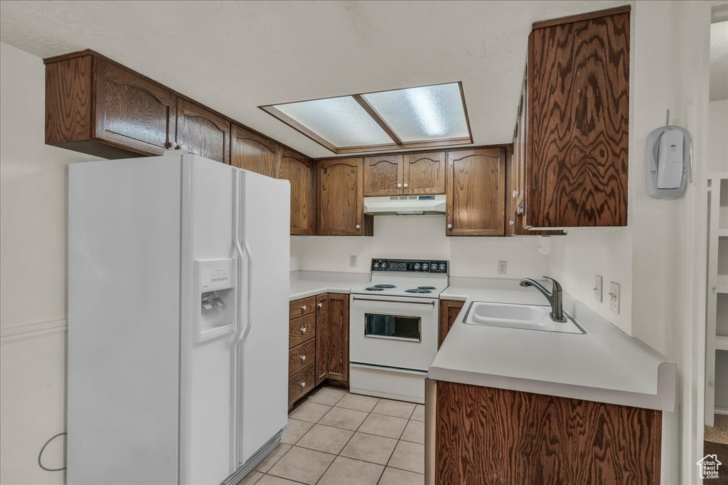 Kitchen with white appliances, a sink, under cabinet range hood, light tile patterned flooring, and light countertops