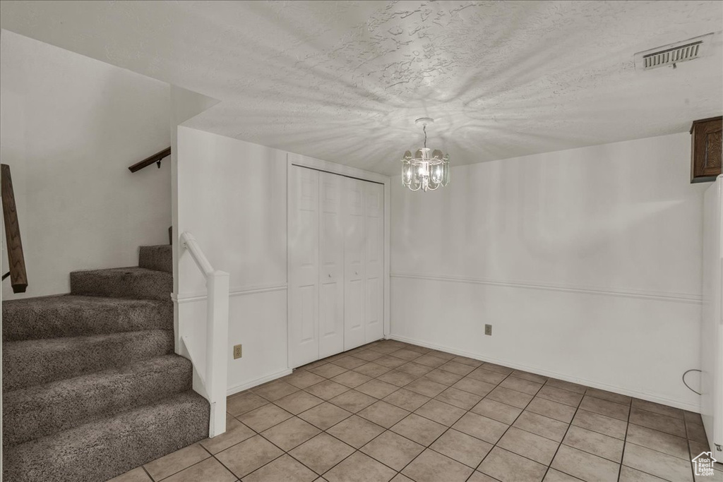 Unfurnished dining area with stairs, a chandelier, and light tile patterned floors
