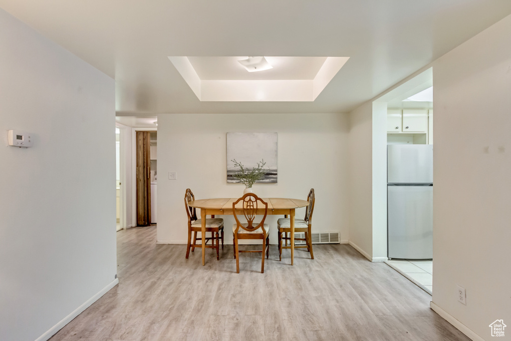 Dining space with a tray ceiling, light wood-type flooring, visible vents, and baseboards
