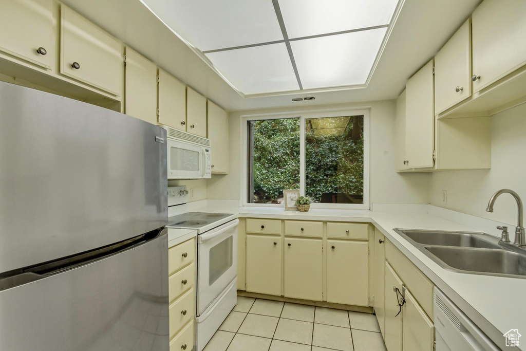 Kitchen with light tile patterned floors, cream cabinets, white appliances, a sink, and light countertops