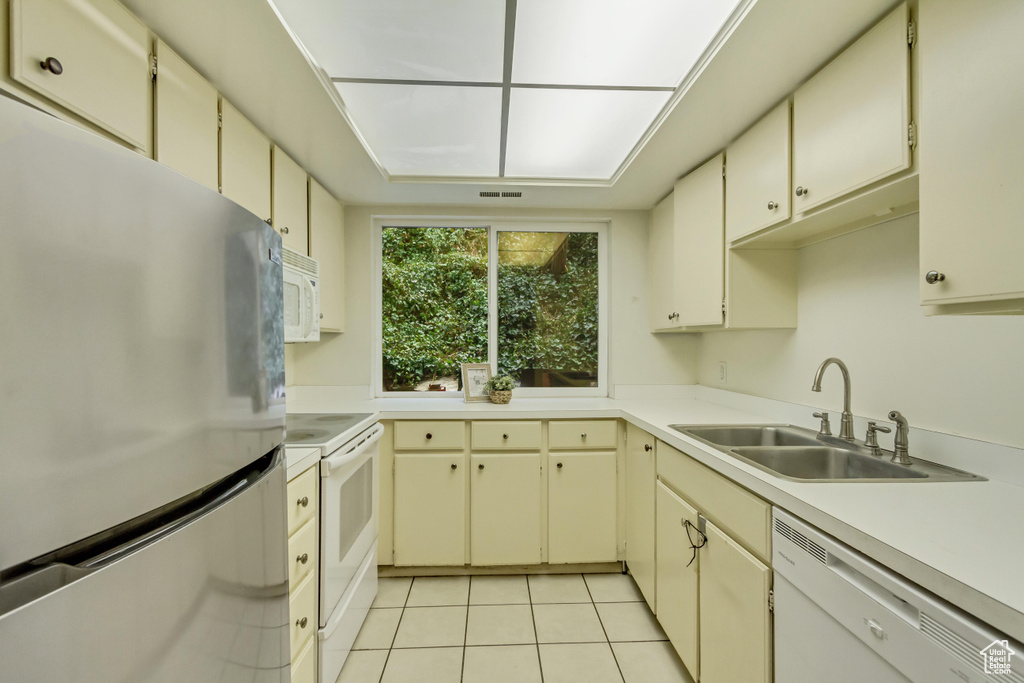 Kitchen with light countertops, white appliances, a sink, and cream cabinetry