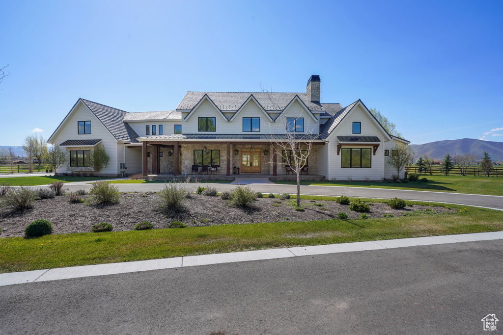 View of front facade featuring covered porch, a chimney, fence, a front lawn, and a standing seam roof