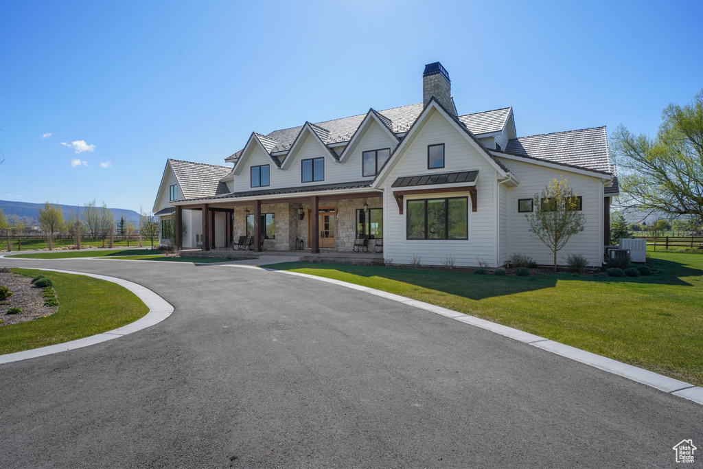 Modern farmhouse style home featuring a chimney, a standing seam roof, metal roof, a porch, and a front lawn
