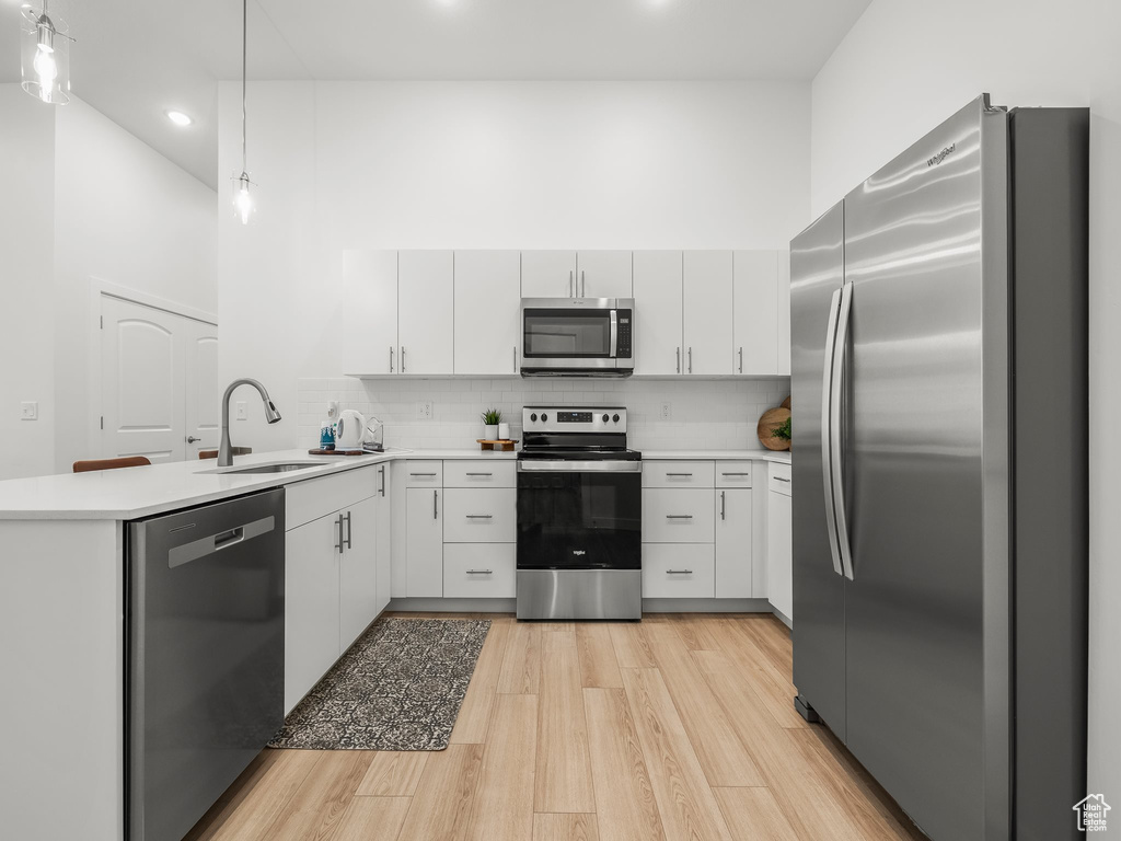 Kitchen featuring stainless steel appliances, a sink, a peninsula, recessed lighting, and light wood-type flooring