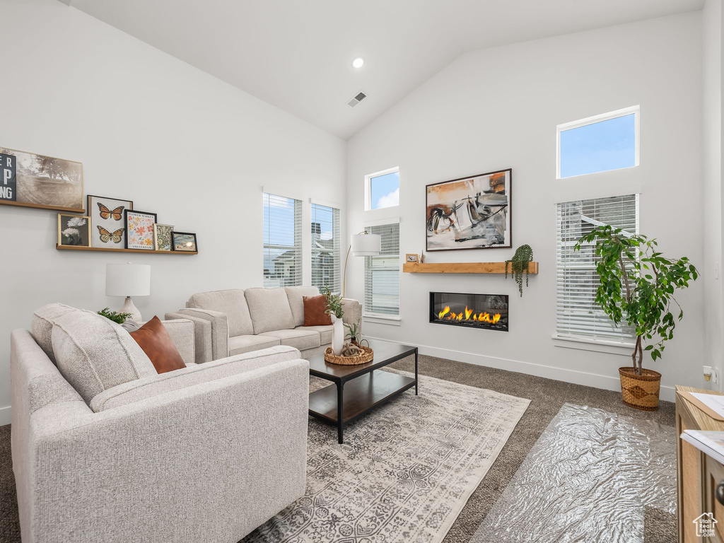 Carpeted living room with baseboards, high vaulted ceiling, a glass covered fireplace, and recessed lighting
