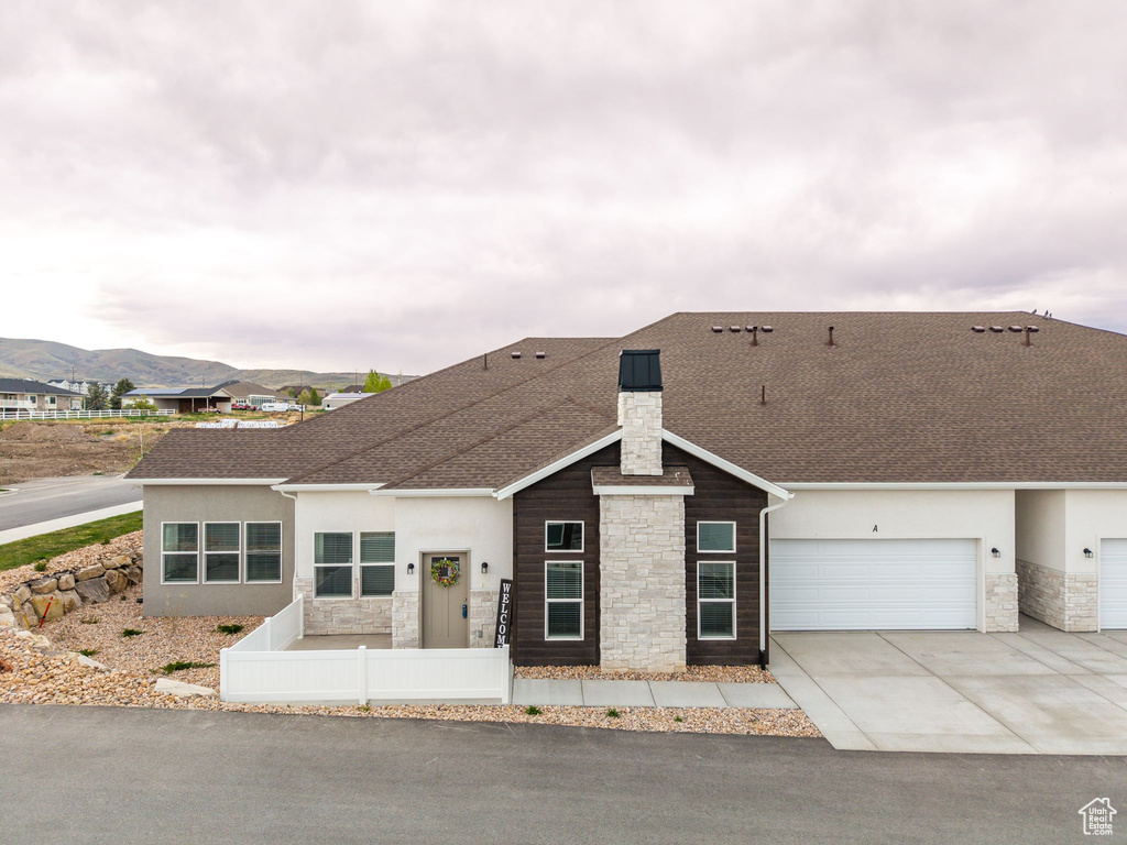 Ranch-style house featuring stone siding, a chimney, driveway, and stucco siding