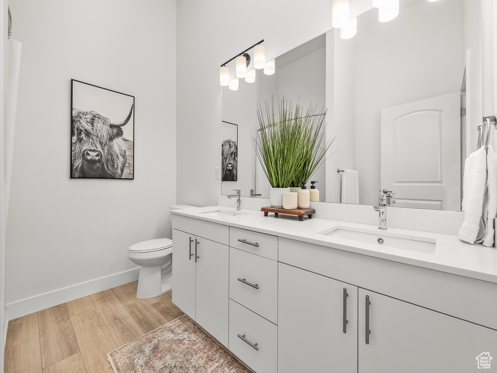 Full bathroom with wood finished floors, double vanity, baseboards, and toilet