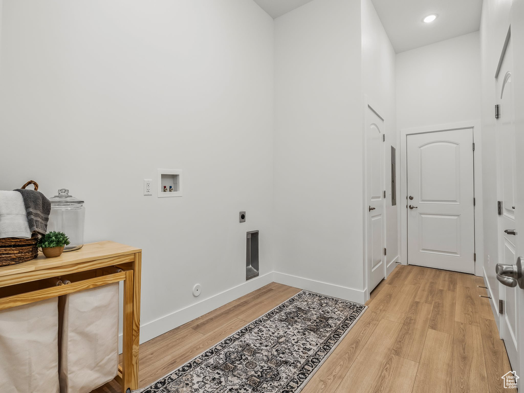 Clothes washing area with electric dryer hookup, hookup for a washing machine, light wood-type flooring, baseboards, and hookup for a gas dryer