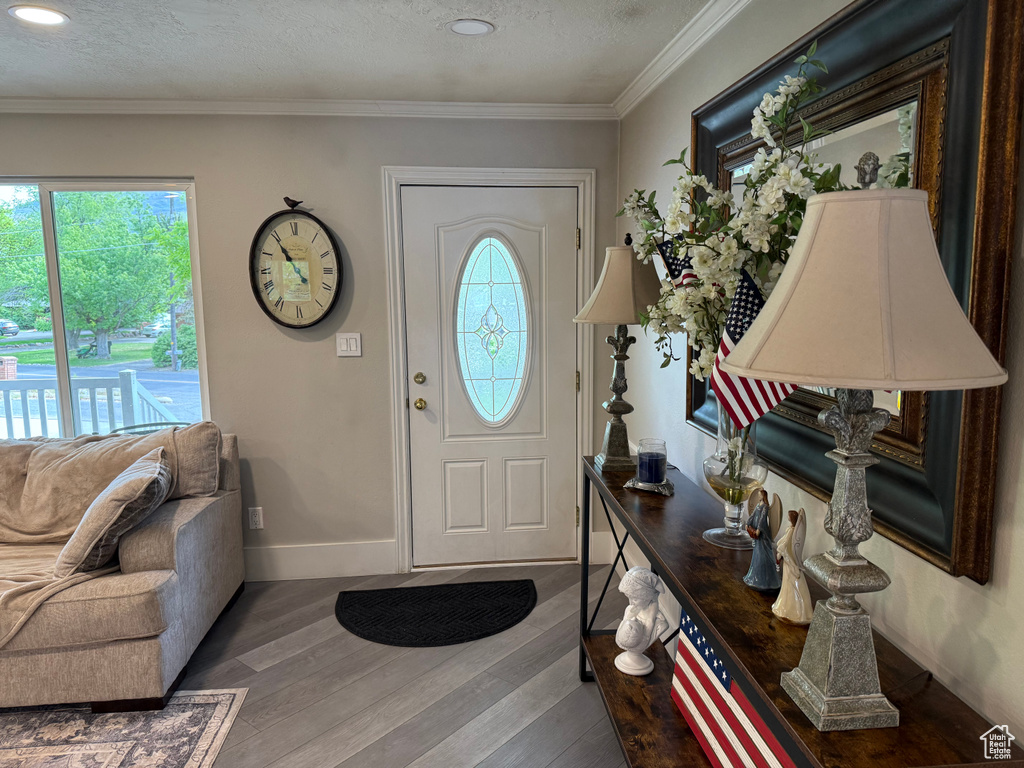 Foyer entrance featuring plenty of natural light, wood finished floors, baseboards, a textured ceiling, and ornamental molding
