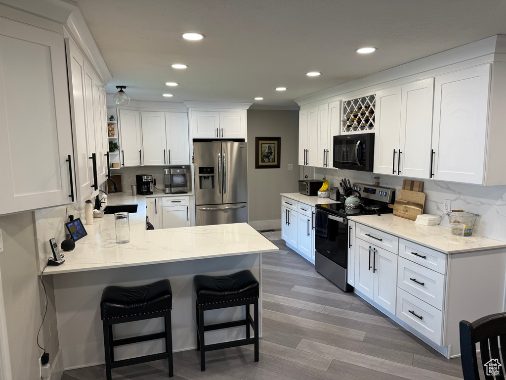 Kitchen featuring stainless steel appliances, a peninsula, tasteful backsplash, white cabinetry, and recessed lighting