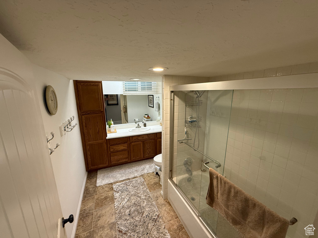 Full bath with enclosed tub / shower combo, vanity, baseboards, toilet, and stone finish flooring