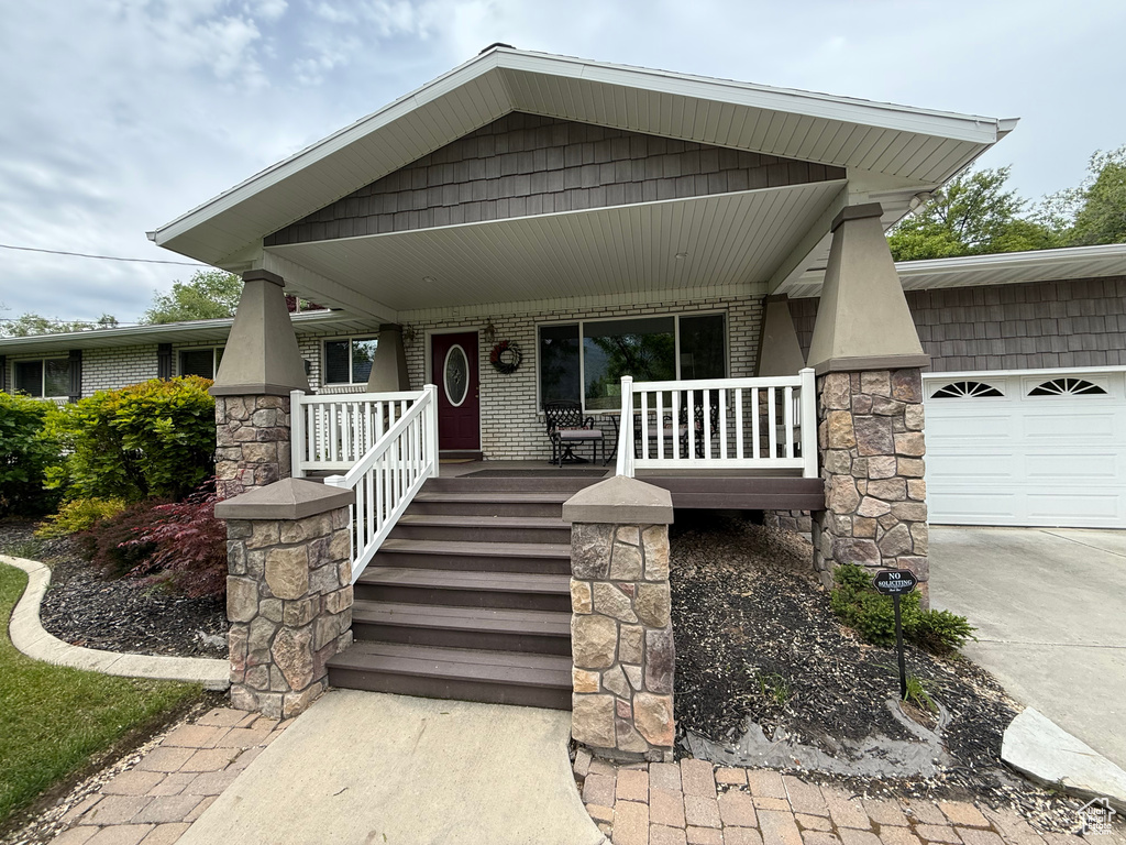 View of front of home featuring covered porch, an attached garage, concrete driveway, and brick siding
