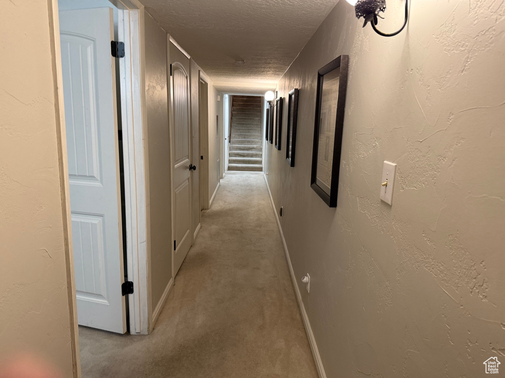 Hall with light colored carpet, a textured ceiling, and baseboards