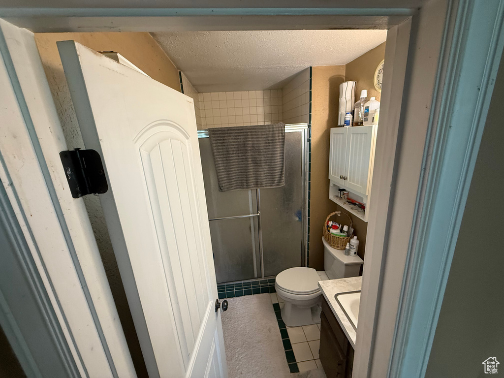Bathroom featuring a shower stall, a textured ceiling, toilet, tile patterned flooring, and vanity