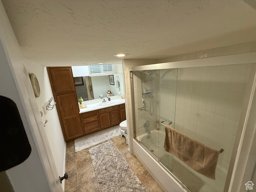 Full bath featuring toilet, vanity, a textured ceiling, and enclosed tub / shower combo