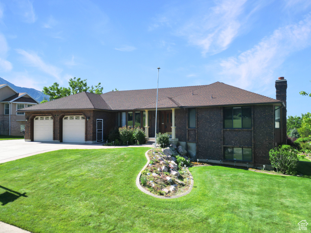 View of front of home featuring an attached garage, a chimney, a front yard, and driveway