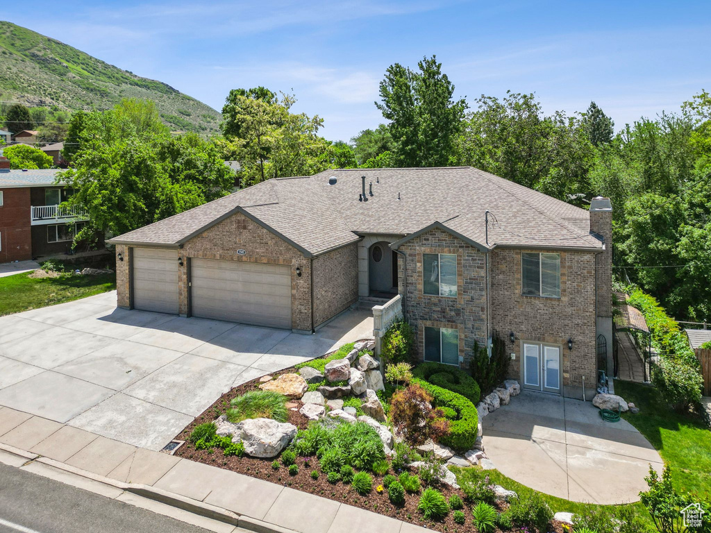 View of front of property featuring a garage, driveway, a chimney, a mountain view, and roof with shingles