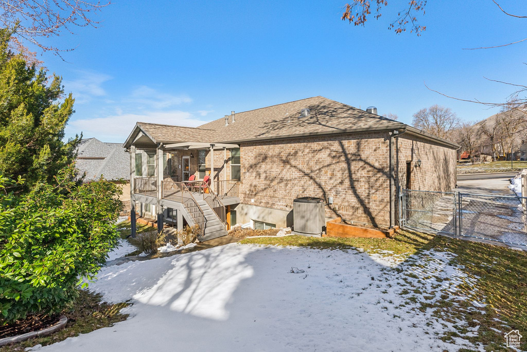 Snow covered back of property with a gate, fence, stairway, and brick siding