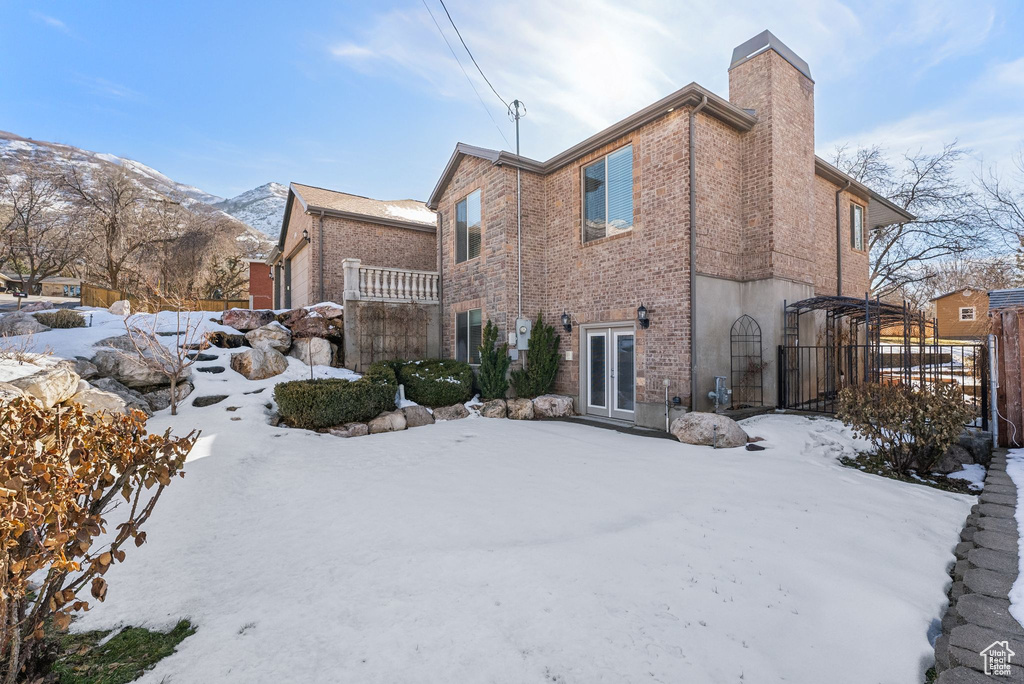 Snow covered house with brick siding, a mountain view, a chimney, and fence