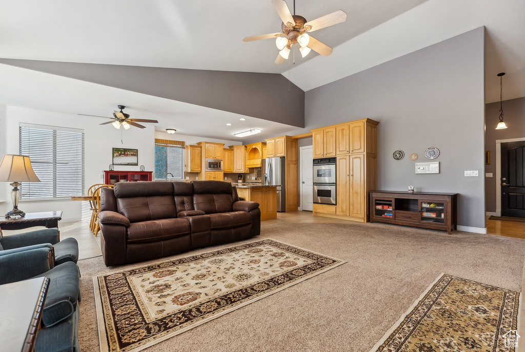 Living area featuring baseboards, high vaulted ceiling, a ceiling fan, and light colored carpet