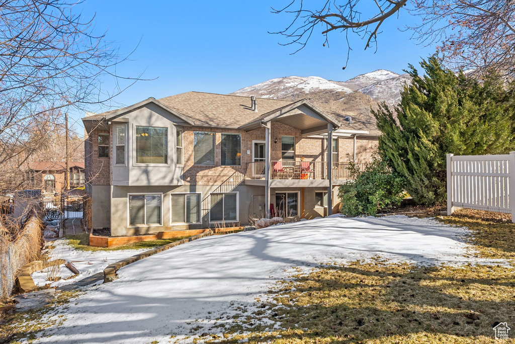 View of front of property with driveway, a balcony, fence, a mountain view, and stucco siding