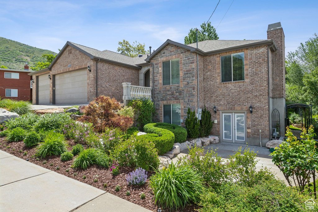 View of front facade featuring a chimney, brick siding, a garage, french doors, and a mountain view