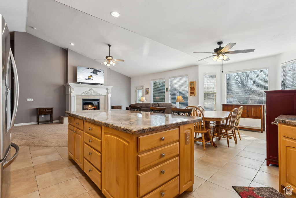 Kitchen featuring a kitchen island, a ceiling fan, open floor plan, freestanding refrigerator, and a glass covered fireplace