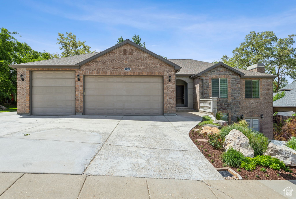 View of front of house featuring brick siding, an attached garage, concrete driveway, and a chimney