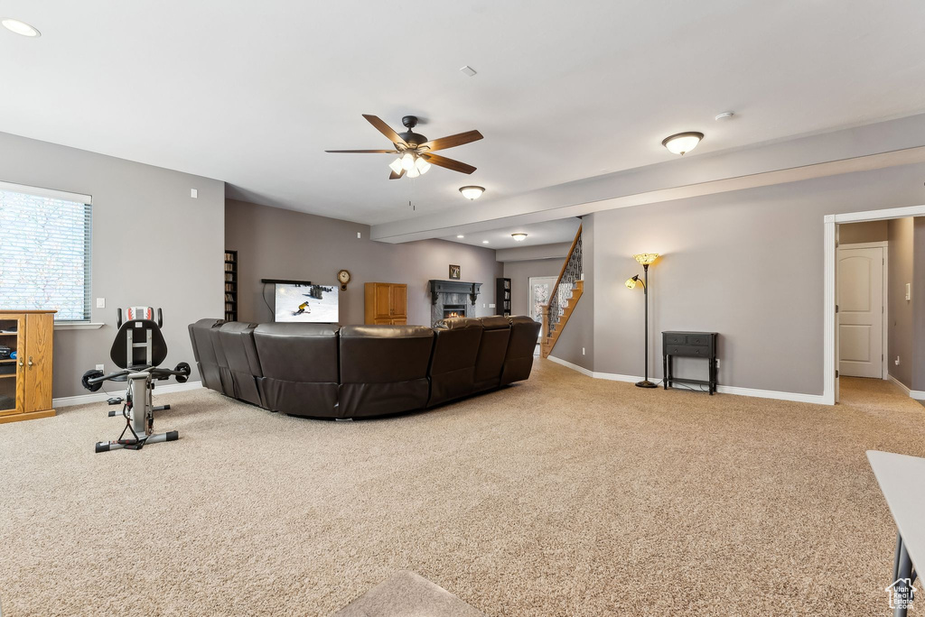 Carpeted living room featuring a warm lit fireplace, baseboards, stairway, and a ceiling fan