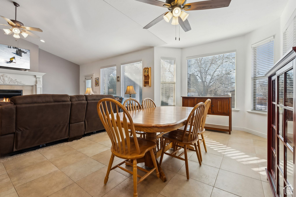Dining area with lofted ceiling, a lit fireplace, light tile patterned floors, and a ceiling fan