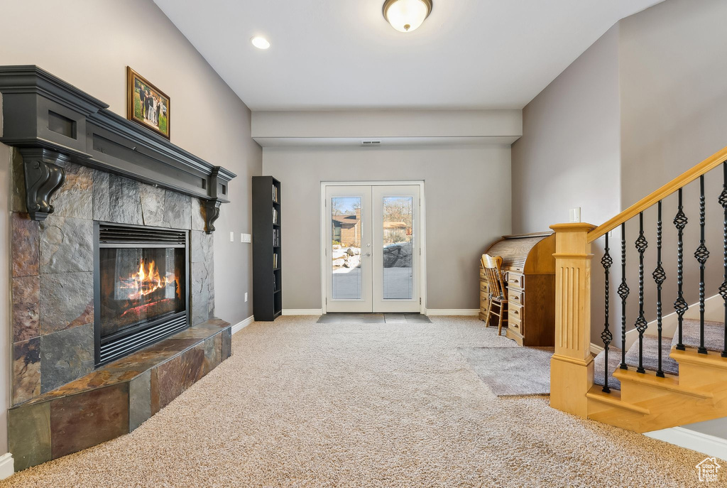 Living area with a tile fireplace, baseboards, stairs, french doors, and carpet