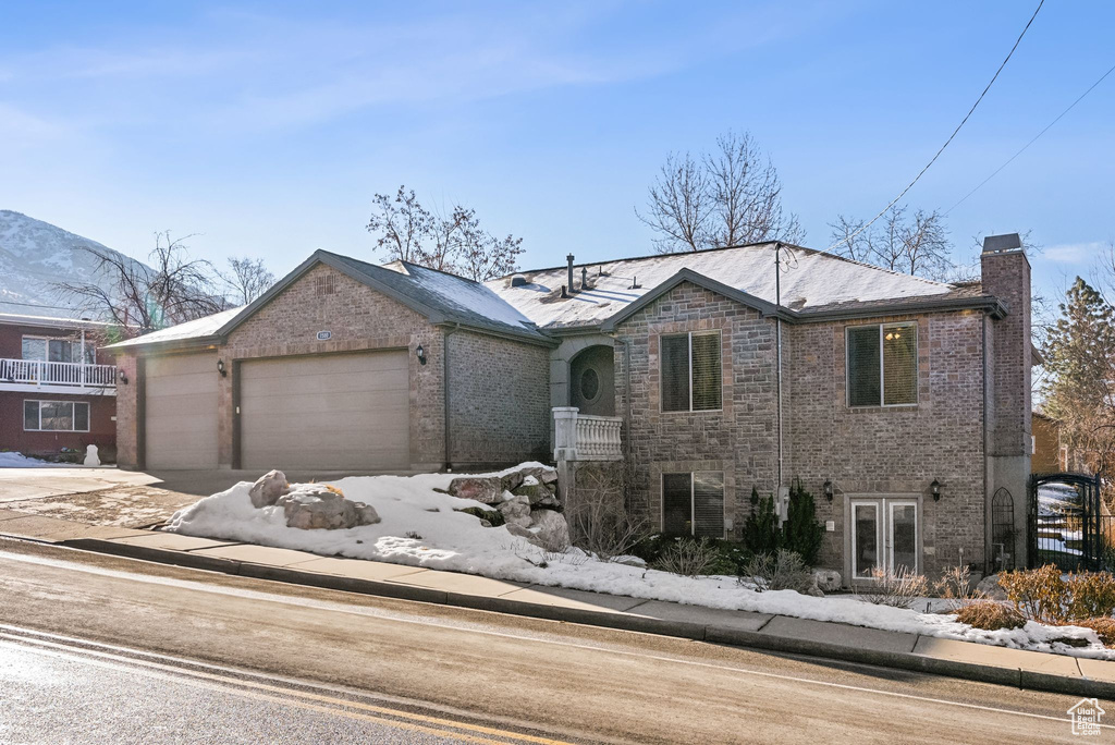 View of front of property featuring an attached garage, a mountain view, brick siding, driveway, and a chimney