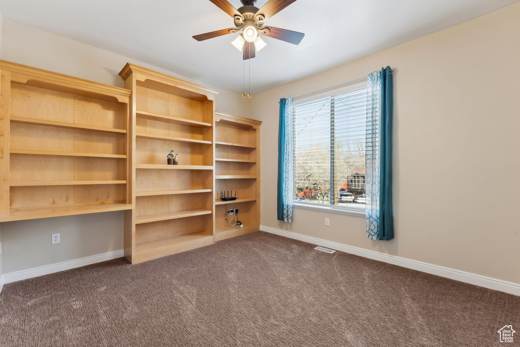 Spare room featuring dark colored carpet, visible vents, built in desk, and baseboards