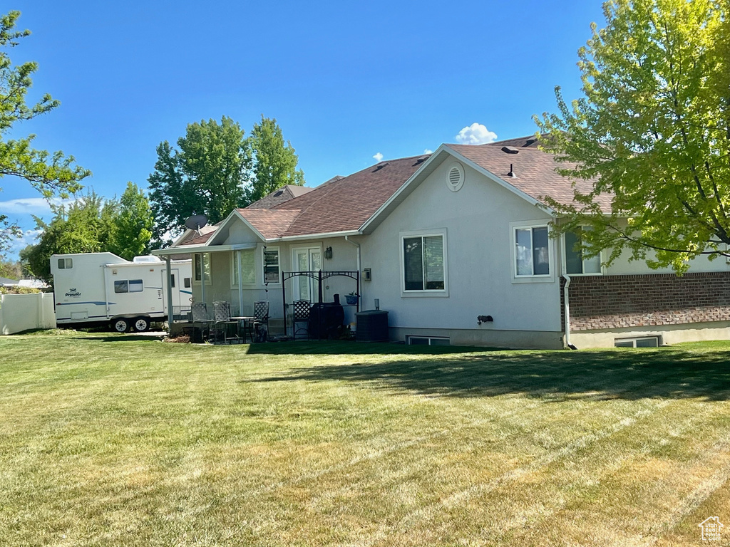 Back of house featuring a lawn, roof with shingles, central AC unit, and stucco siding