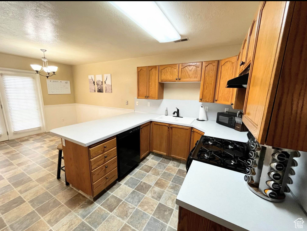 Kitchen with pendant lighting, a sink, under cabinet range hood, a peninsula, and black appliances