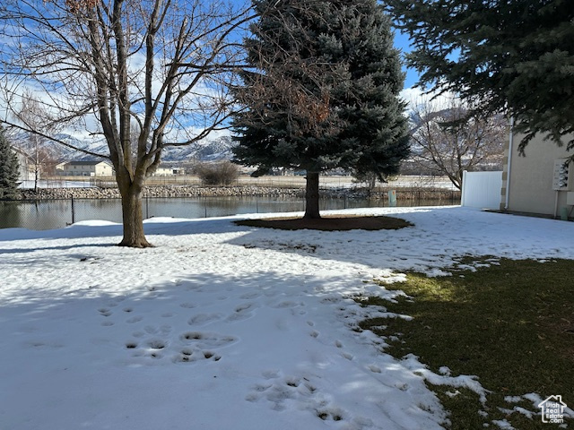 Yard layered in snow with a water view and fence