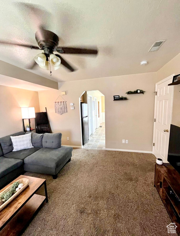 Living room featuring visible vents, arched walkways, a textured ceiling, and light colored carpet