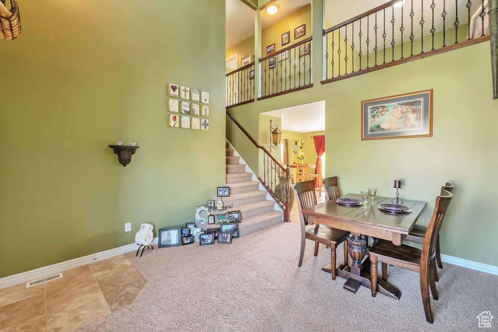 Dining space featuring carpet flooring, a towering ceiling, visible vents, baseboards, and stairway