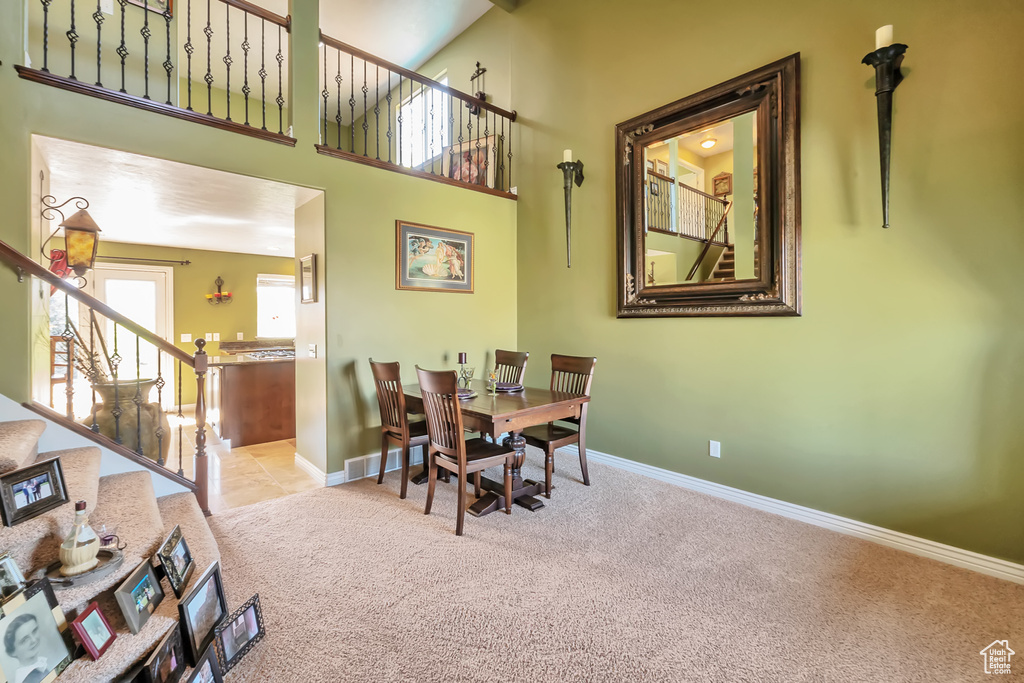 Dining room with light carpet, a high ceiling, visible vents, baseboards, and stairway
