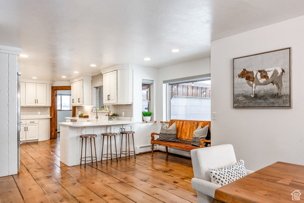 Kitchen featuring a breakfast bar area, light wood-type flooring, a sink, a peninsula, and white cabinetry
