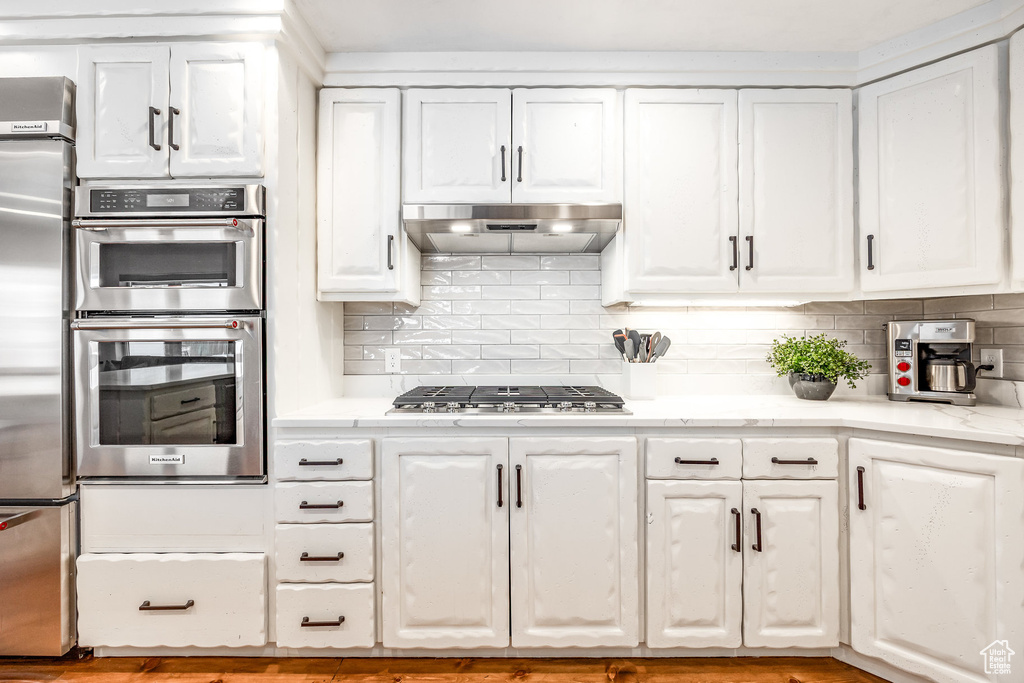 Kitchen featuring under cabinet range hood, stainless steel appliances, white cabinets, and tasteful backsplash