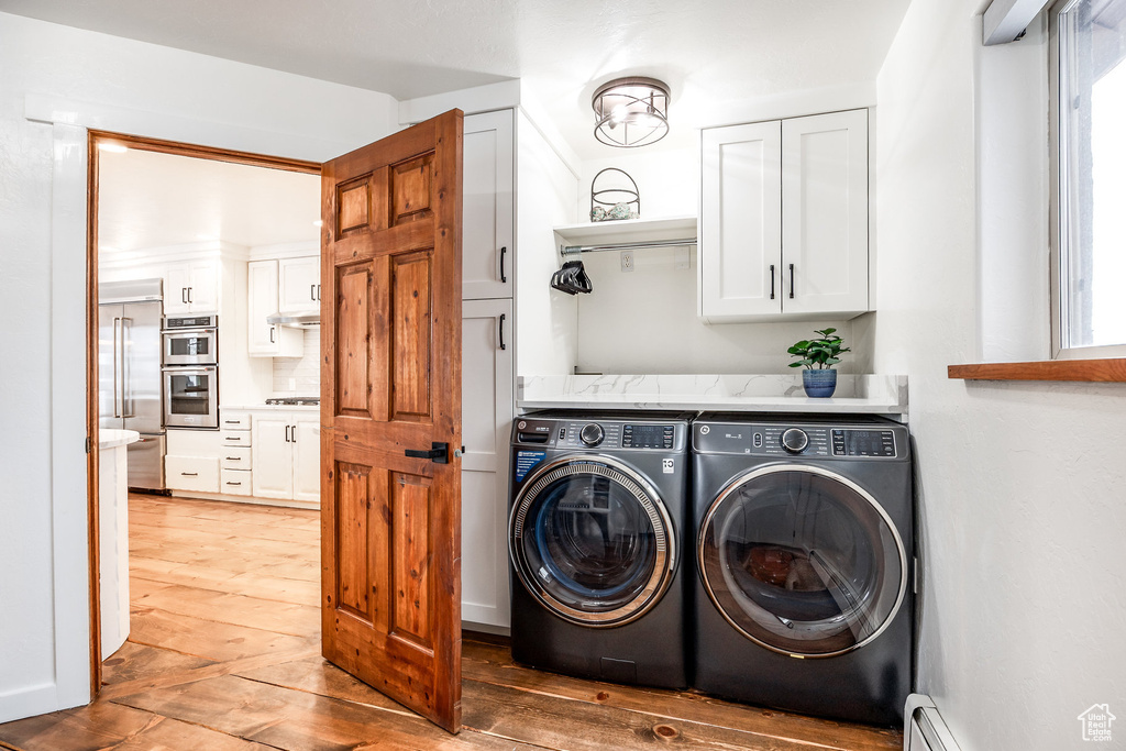 Laundry room featuring a baseboard radiator, cabinet space, wood-type flooring, and independent washer and dryer