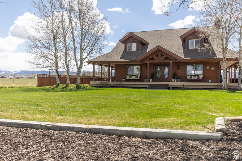 Rear view of property featuring a porch, a chimney, roof with shingles, fence, and a yard