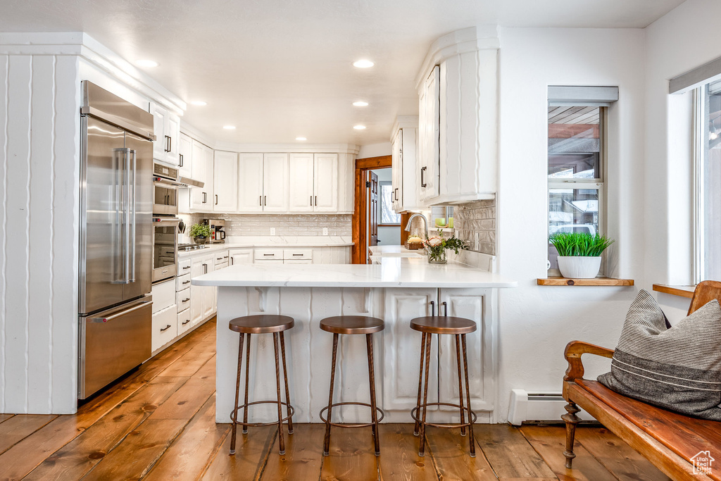 Kitchen with built in fridge, a sink, light wood finished floors, a peninsula, and white cabinetry