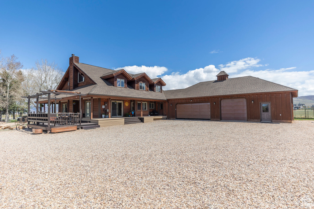 View of front of property with a porch, driveway, a chimney, roof with shingles, and a garage
