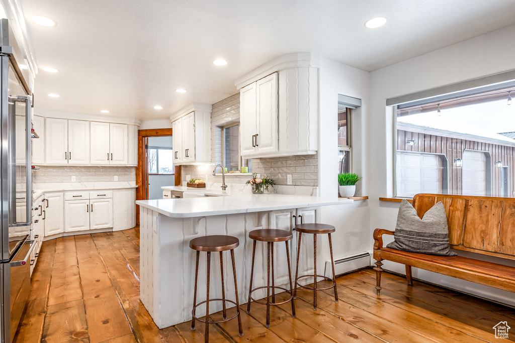 Kitchen featuring light countertops, a peninsula, white cabinets, and light wood-style flooring
