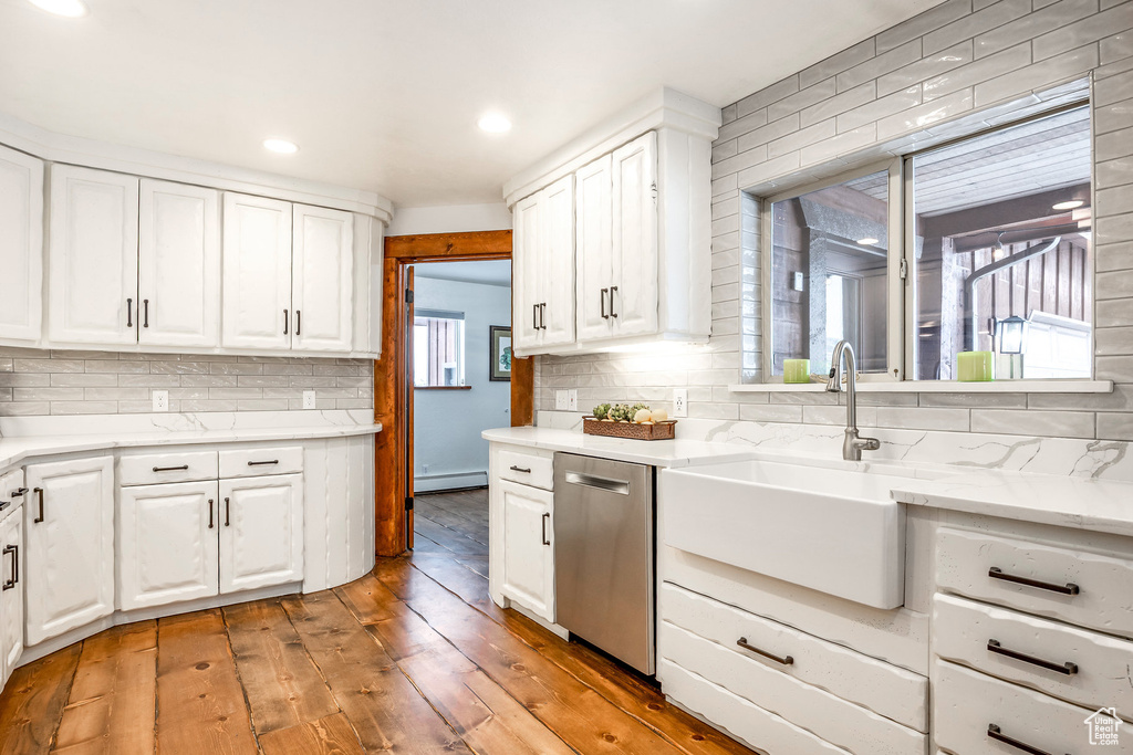 Kitchen with stainless steel dishwasher, backsplash, white cabinets, and a sink