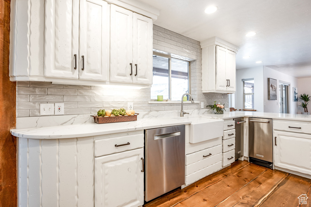 Kitchen featuring decorative backsplash, wood finished floors, dishwasher, a sink, and white cabinets