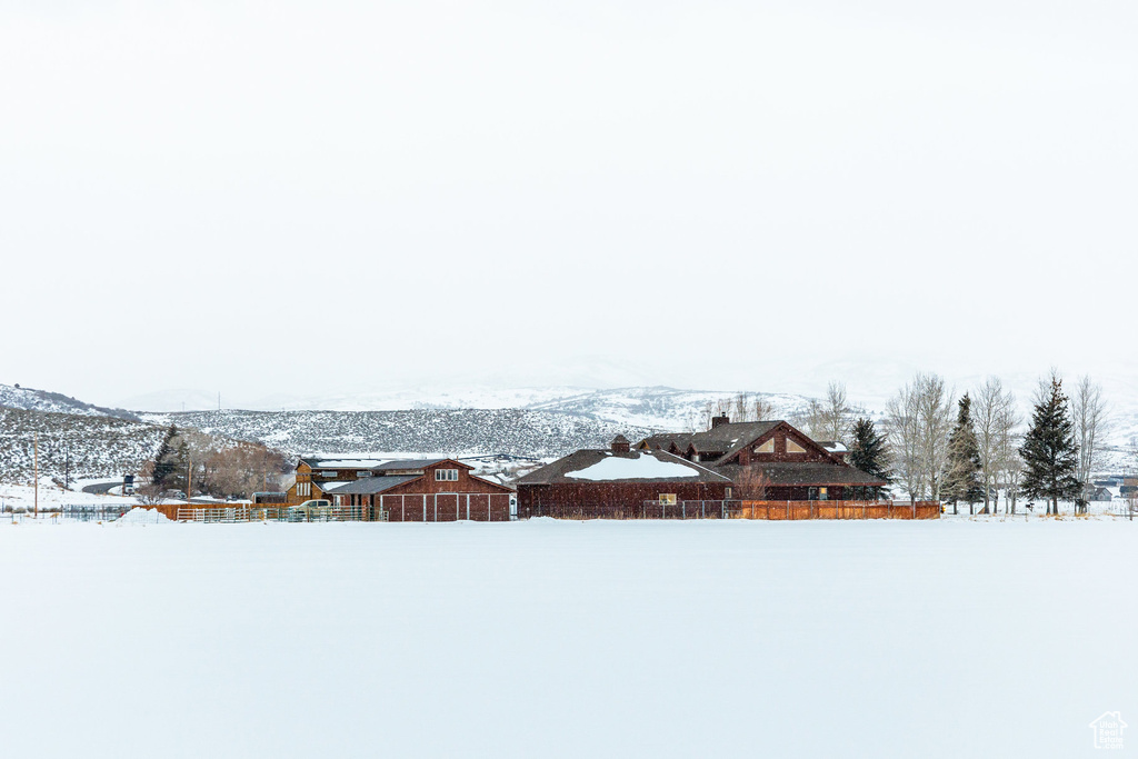Yard covered in snow featuring a barn, a mountain view, and an outbuilding