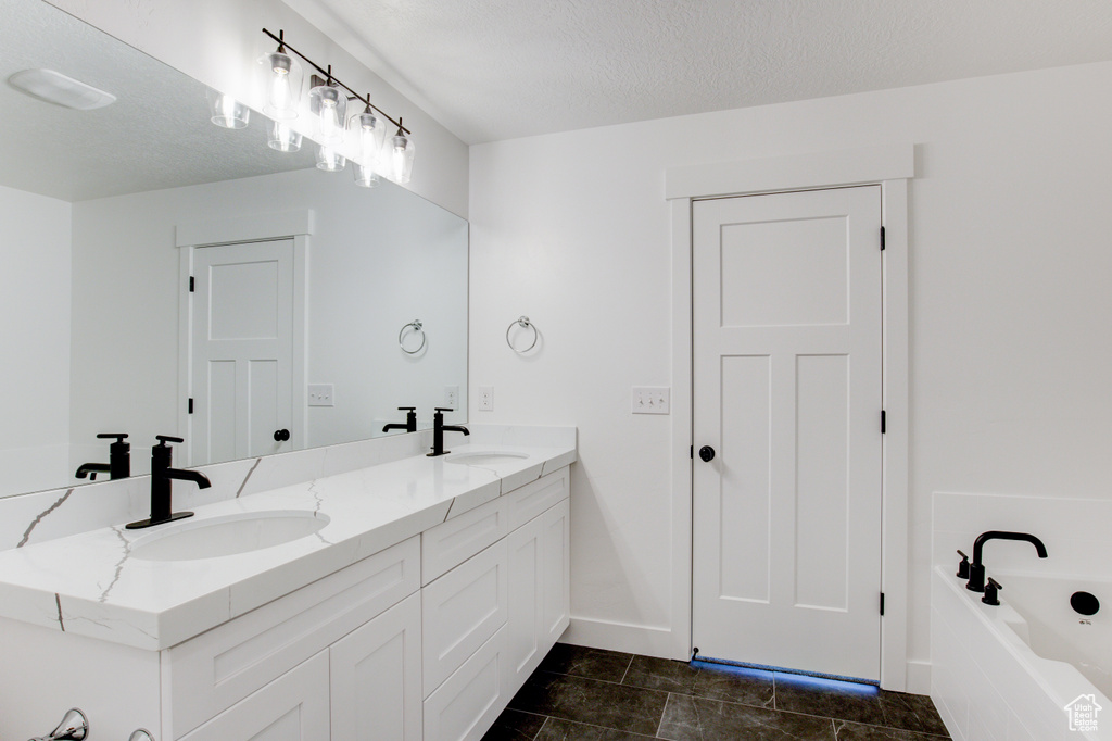 Full bath with double vanity, a tub, a textured ceiling, and a sink